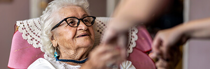 Female home carer supporting old woman to stand up from the armchair