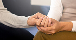 Two people sitting close together and clasping hands.