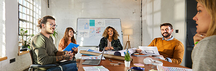 Group of smiling people in meeting around table with laptops and business documents