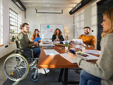 Group of smiling people in meeting around table with laptops and business documents