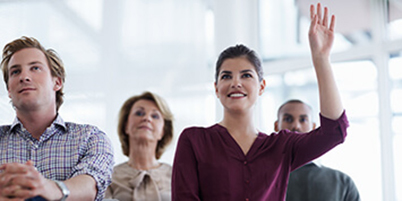 Smiling woman in small group pf seated people with hand raised to ask a question