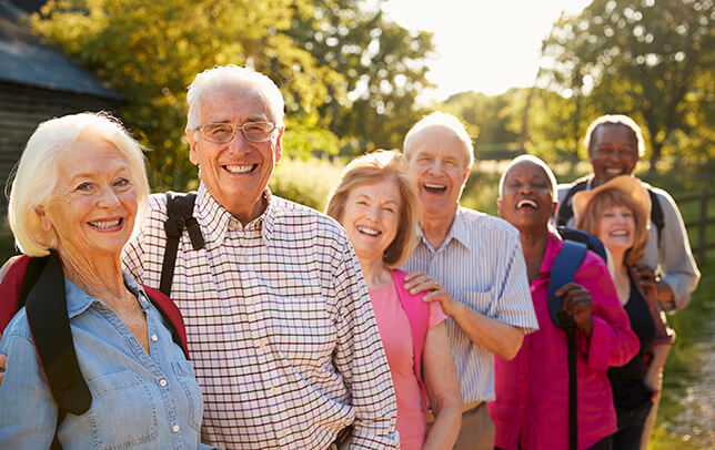 Group of senior friends out for a walk pose in a row along a fence