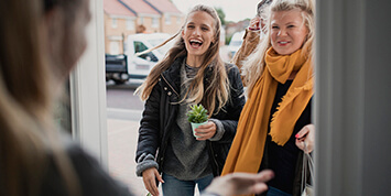 Person standing at an open door talking to two smiling women