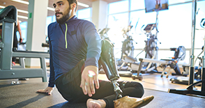 Bearded athlete with amputee leg sitting on the floor and resting in health club