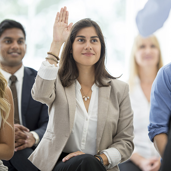 Woman in training group seated with hand raised to ask a question