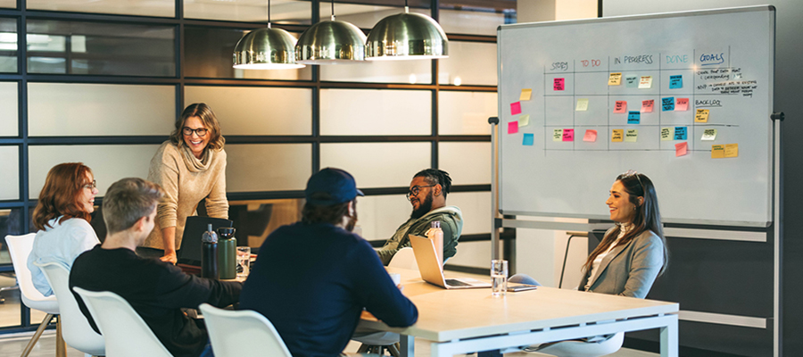 Business people in a boardroom engage in a creative discussion, exchanging ideas with a confident leader facilitating the meeting. The happy team represents successful collaboration and a modern tech company's productive work environment.